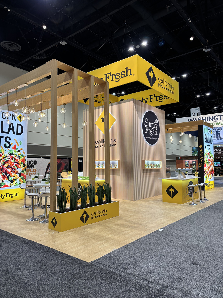Simply Fresh and California Pizza Kitchen 30x50 trade show exhibit at the 2026 Global Produce & Floral Show, featuring yellow overhead signage, wood structures, pendant lighting, and product displays.