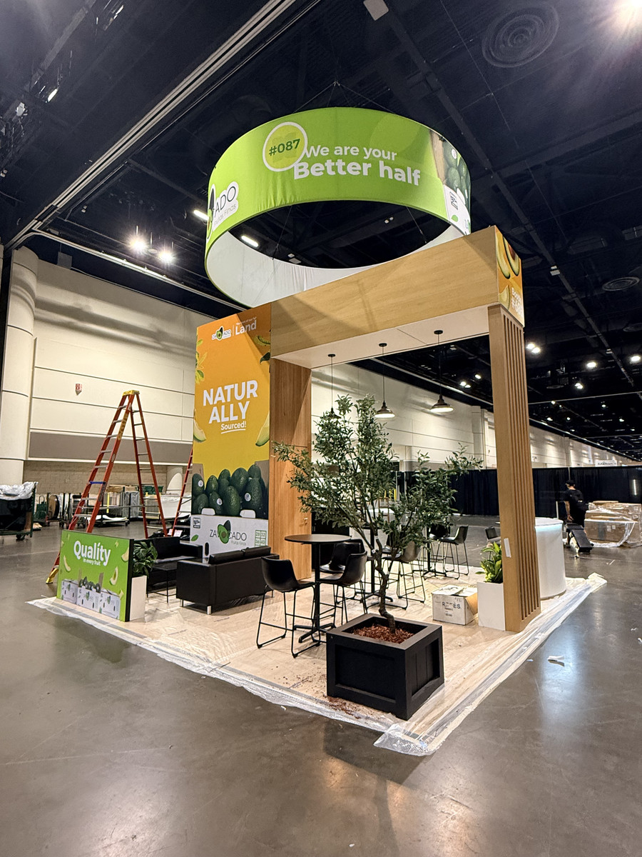Zavocado Frutas Finas 20x20 trade show exhibit at Global Produce Show 2026, featuring green circular overhead signage, natural wood framing, avocado graphics, and meeting areas.